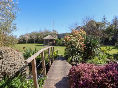 A garden with a wooden bridge and flowering plants at Pillars in Barnstaple