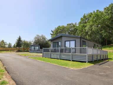 Two holiday lodges with decking and trees at Cedar Lodge 3 Bedrooms with hot tub Delamere