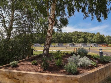 A garden area with a planter and caravans in the background at Cedar Lodge 3 Bedrooms with hot tub Delamere