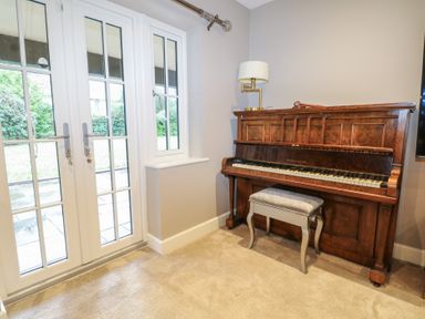 A music room with a piano and windows at Woodlands house in Ringwood