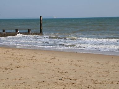 A beach with sand and a pier extending into the ocean at Woodlands House in Ringwood