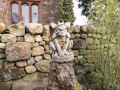 A stone gargoyle statue on a wooden stump near a stone wall at Dunfell Shepherd's Hut in Appleby-In-Westmorland