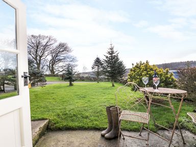A garden view with a metal table and chairs and a bottle of wine and glasses on the table at Honey Bee Cottage in Staintondale