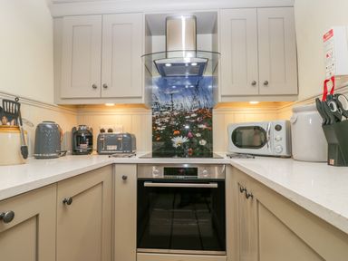 A kitchen with beige cabinets a stove with a floral backsplash and various small appliances including a toaster coffee maker and microwave at Honey Bee Cottage in Staintondale