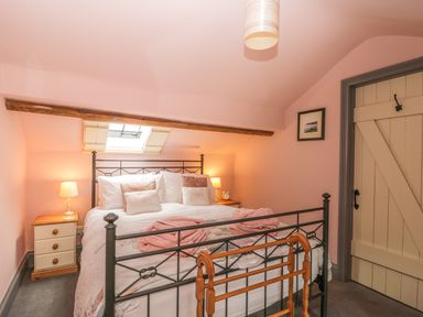 A bedroom with a metal bed frame two bedside tables with lamps a wooden door and a skylight window at Honey Bee Cottage in Staintondale