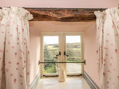 A window with floral curtains and a ceramic pitcher on the windowsill showing a countryside view at Honey Bee Cottage in Staintondale