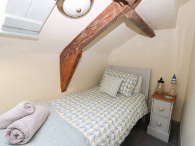 A small bedroom with a single bed under a sloped ceiling with wooden beams and a nightstand at Honey Bee Cottage in Staintondale