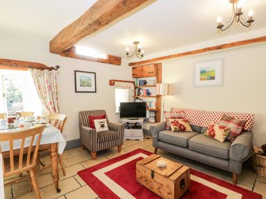 A living room with a gray sofa armchair dining table and wooden beams at Honey Bee Cottage in Staintondale