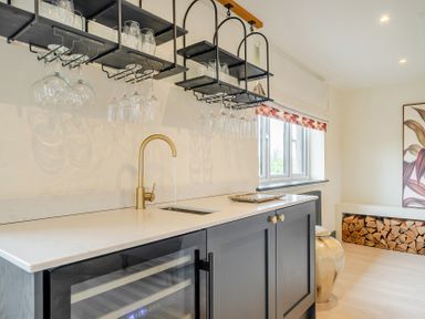A kitchen with a sink, wine cooler and shelves holding glasses at Bell House Llanfechell