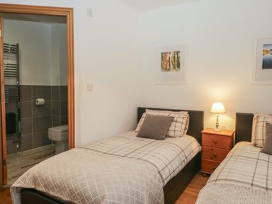 A bedroom with two beds and a bathroom door at Newlands Cottage in Keswick