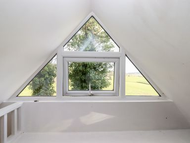 A loft with a triangular window overlooking a tree and field at The Old Telephone Exchange in Exeter