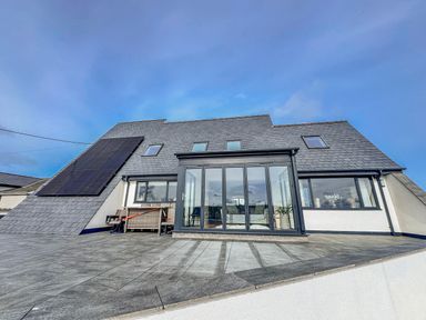 A modern building with solar panels and patio at Pengarnedd Amlwch