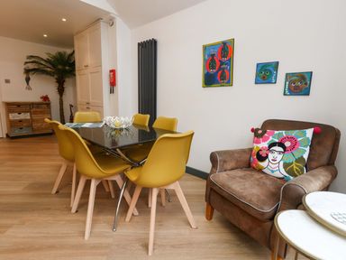 A dining room with a table and chairs, a sofa, and wall art at Still Waters in Weymouth