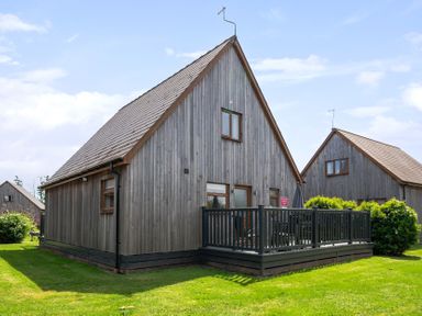 A wooden cabin with a deck and grass outside at James Ville Marina Lodge 8 Brigg