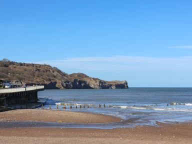 A beach with a cliff and a pier at South Villa in Sandsend near Whitby