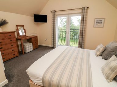 A bedroom with a bed, dresser, mirror, and television at James Ville Marina Lodge 14, Brigg