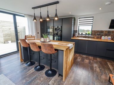 A kitchen with a large island and bar stools at The Joiners Cottage in Birling near Warkworth