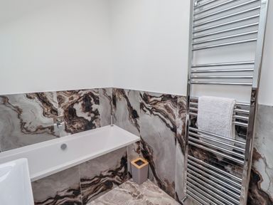A bathroom with a bathtub and towel radiator at The Joiners Cottage in Birling near Warkworth