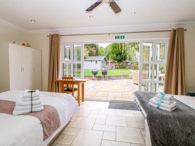 A bedroom with two beds and a table leading to a patio at Oldfields Bury St Edmunds