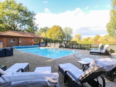 An outdoor swimming pool area with chairs and a cabin at Oldfields in Bury St Edmunds