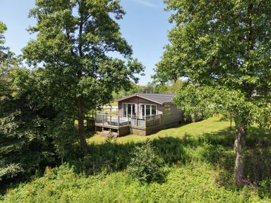 A cabin with a deck surrounded by trees at 20 Meadow Retreat in Dobwalls