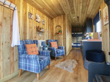 A living room with blue chairs and a kitchen area at The Suffolk in Knutsford