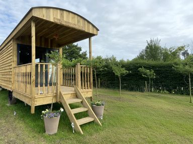 A wooden cabin with steps and planters at The Suffolk Hut in Lower Peover, Cheshire