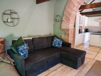 A living room with a sofa and kitchen area at Carwinley Mill House Cottage near Longtown