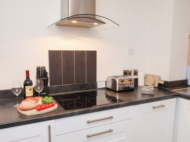 A kitchen with a wine bottle, glasses, and vegetables on the counter at One Union Mill - garden apartment in Whitby