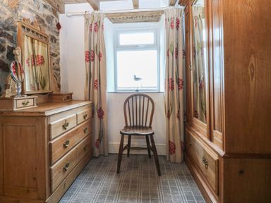 A bedroom with a wooden dresser, chair, and curtains at Parc y Brenin Holidays, Abersoch