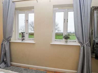 Two windows with curtains and a vase on the sill at Ivy Barn, Norwich