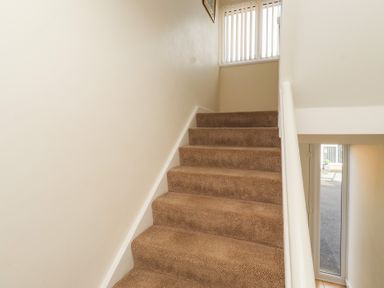 A staircase with carpet leading to a window and door at Kittiwake at No 20 Seahouses