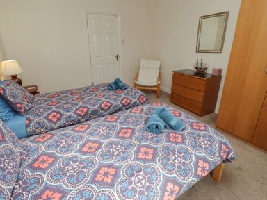 A bedroom with two beds, a lamp, and a dresser at Kittiwake at No 20 Seahouses
