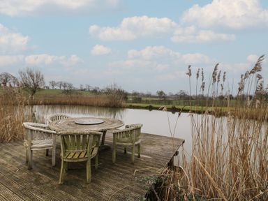 An outdoor space with a table and chairs by the water at The Barn on The Lagoon in Droitwich