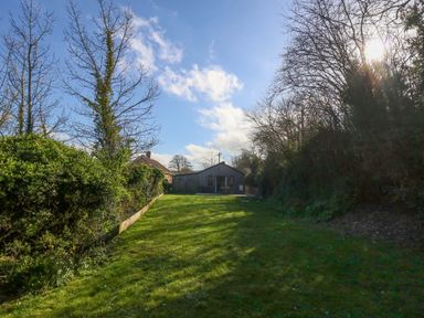 A garden with grass, trees, and a house in the distance at The Pebble in Dorchester