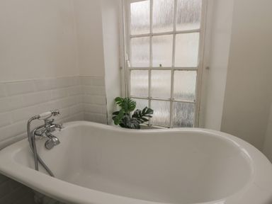 A bathroom with a bathtub and window at 1 Alpha Cottages in Tenby