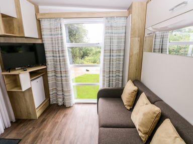 A living room with a television, sofa, and window at The Pod in Ferryside