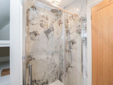 A shower with glass door and marble wall tiles at Paddock View in Stow-On-The-Wold
