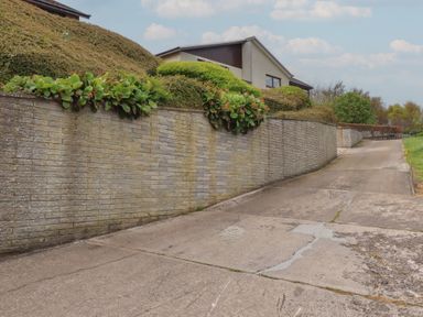 A driveway with a brick wall and hedges at Tigh-Na-Mara Retreat