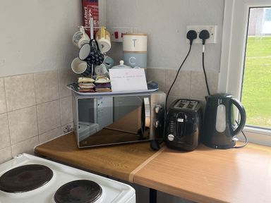 A kitchen with a microwave, toaster, kettle, mugs, and sugar packets at Chalet - Buckland 16 in Bideford