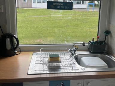 A kitchen sink with a dish rack and cleaning supplies at Chalet - Buckland 16 in Bideford