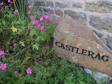 A stone with the name Castlerag surrounded by flowers at Castlerag in Parkend
