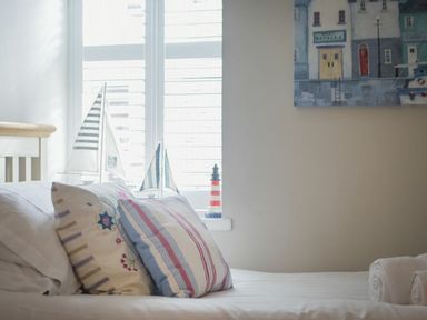 A bedroom with pillows on a bed and sailboat models on a window sill at Juniper Cottage