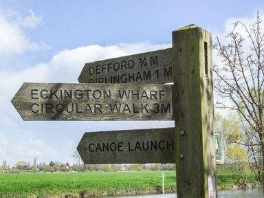 A wooden signpost with directions to Defford 3 quarters mile Birlngham 1 mile Eckington Wharf Circular Walk 3 miles and Canoe Launch in a rural area