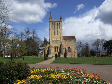 A stone church with a tower in a park with flower beds and trees at Lakeview Yurt in Beckford near Tewkesbury