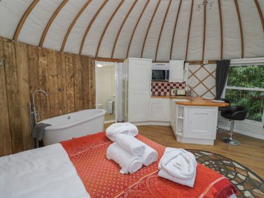 A yurt interior with a bed, rolled towels, a freestanding bathtub, kitchenette, and a bathroom door at Lakeview Yurt in Beckford near Tewkesbury