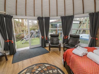 A room with two black chairs a bed with red and orange bedding and folded towels and large windows with dark curtains at Lakeview Yurt in Beckford near Tewkesbury