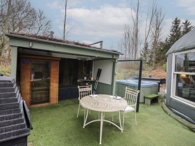 An outdoor area with a round table and two chairs a hot tub a small wooden sauna and a covered seating area at Lakeview Yurt Beckford near Tewkesbury
