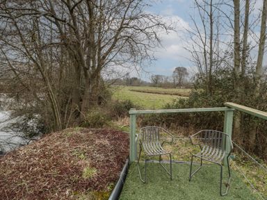 Two metal chairs on a small outdoor deck overlooking a grassy field and trees at Lakeview Yurt in Beckford near Tewkesbury