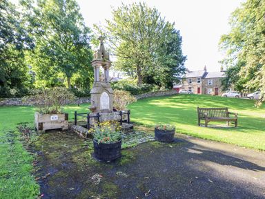 A memorial with flower pots and park benches in a green space at Dove Cottage Hexham